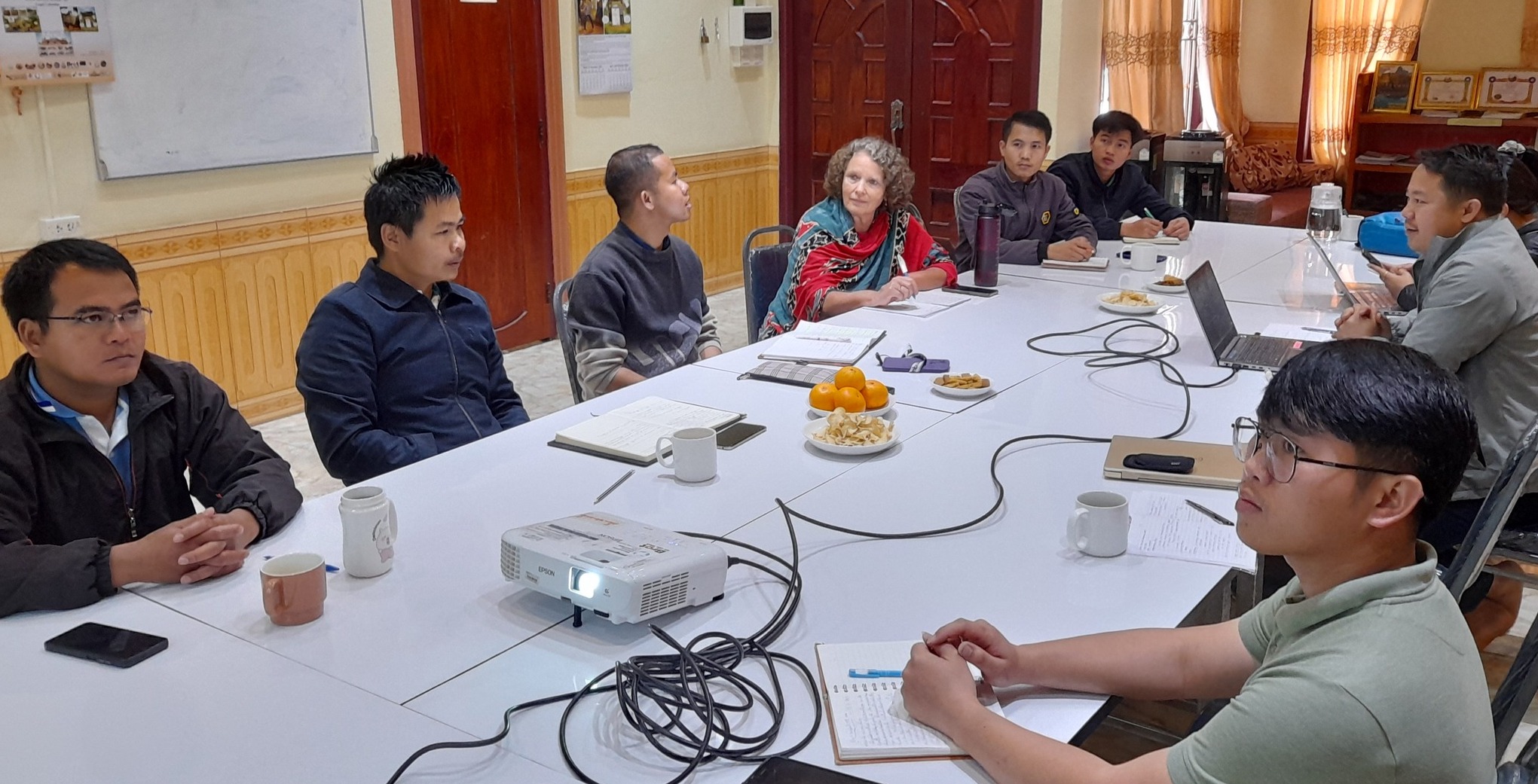 Lao Alumni with Marlies Roth sitting aourn a table with a projector discussing a presentation